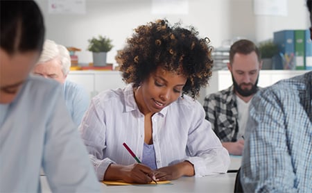 A group of adult learners take notes at their desks