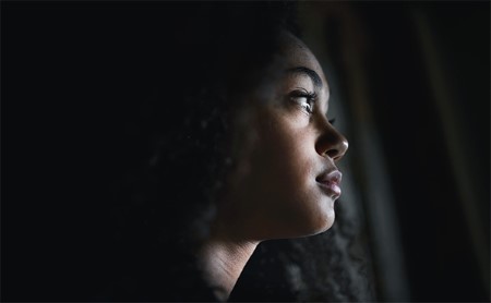 Close-up of a sad young woman in a dark room, looking out the window