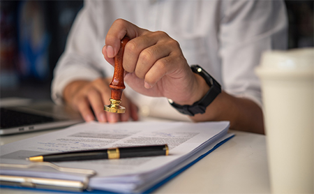 Misection shot of a man at a desk holding a seal (such as one used to stamp hot wax) over a contract