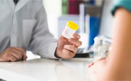 physician-giving-urine-sample-container-to-woman-patient.jpg