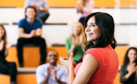 Focus on a woman of color speaking in front of an applauding audience